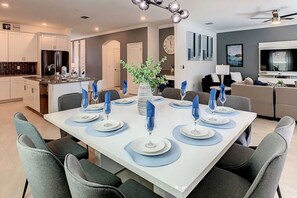 A modern dining area with a white table set for six, surrounded by grey chairs. - Themed Disney Villa 6BD Resort WaterSlide Pool Spa (Kissimmee)