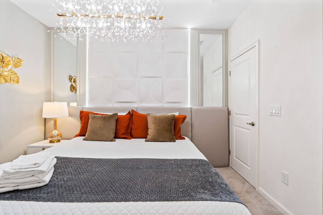 A hotel room with a bed, a chandelier, a nightstand, and a door.