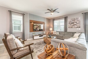 A modern living room with a flat-screen TV, a sofa, a coffee table, and a ceiling fan. - SLEEP 20 DisneyVilla 9BD Resort Waterpark Pool Spa (Kissimmee)