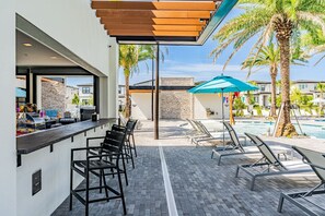 Ein Poolbereich mit Liegestühlen, einer Bar und einer Steinmauer.