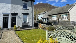 A traditional stone cottage with a thatched roof, a white building with black doors, and a mountain in the background. - Ruby's Cottage -  a house that sleeps 4 guests  in 2 bedrooms (Threlkeld)