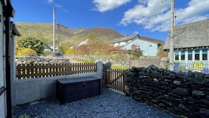 A stone wall, a wooden gate, and a gravel path leading to a house with a light blue exterior. - Ruby's Cottage -  a house that sleeps 4 guests  in 2 bedrooms (Threlkeld)