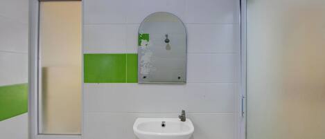 Un baño con un lavamanos blanco, un espejo y azulejos verdes en la pared.