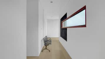 A hallway with a chair, a window with blinds, and a door.