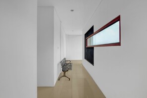 A hallway with a chair, a window with blinds, and a door.
