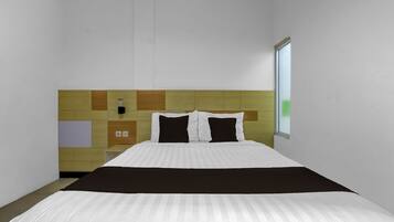 A hotel room with a bed, a headboard with a geometric pattern, a window, and a wall-mounted control panel.