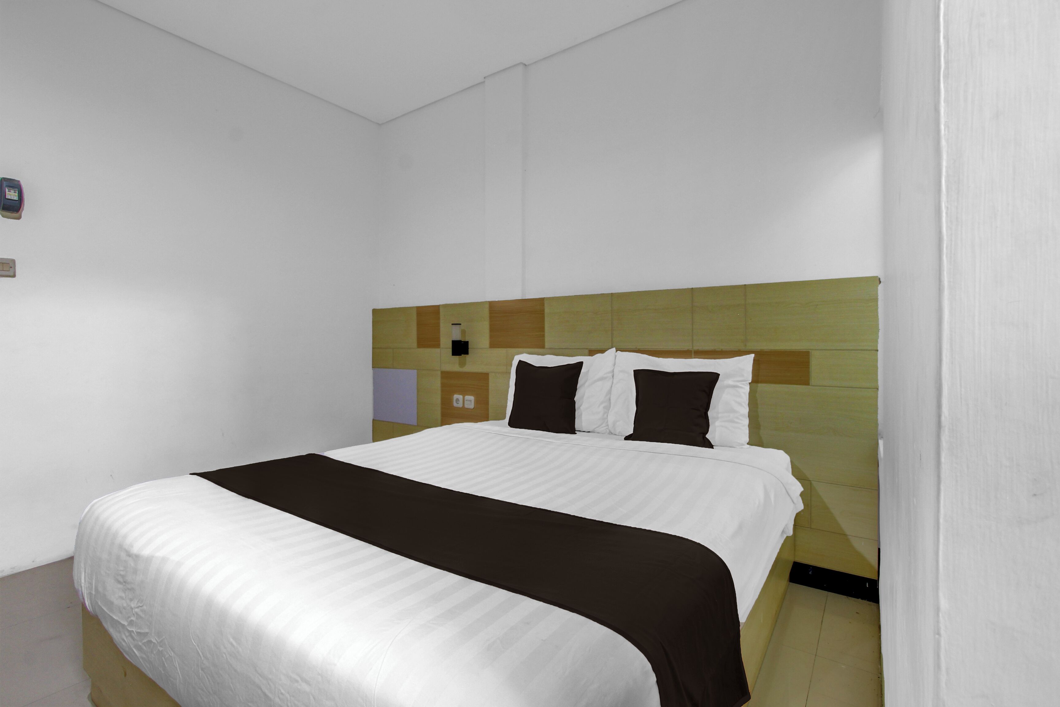 Een hotelkamer met een bed, een hoofdeinde met een geometrisch patroon, een nachtkastje en een lichtschakelaar aan de muur.