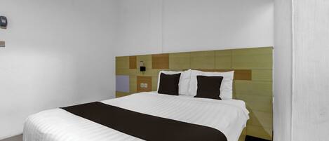 Een hotelkamer met een bed, een hoofdeinde met een geometrisch patroon, een nachtkastje en een lichtschakelaar aan de muur.