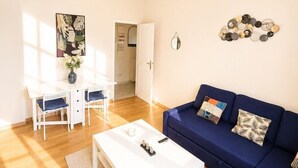 A spacious living room with a white coffee table, blue sofa, and a dining area with a white table and chairs. - Appartement 6 personnes  – Châtellerault (Châtellerault)