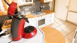 A compact kitchen with white cabinets, a red kettle, and a small dining table. - Appartement 6 personnes  – Châtellerault (Châtellerault)