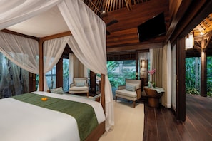 A bedroom with a canopy bed, two chairs, a wooden table, and a TV mounted on the wall. - The Suaka Bali Aga (Seminyak)