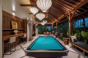 A pool table with a ball, surrounded by bar seating and a wooden ceiling. - The Suaka Bali Aga (Seminyak)