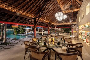 A dining area with a glass table, wicker chairs, and a pool in the background. - The Suaka Bali Aga (Seminyak)