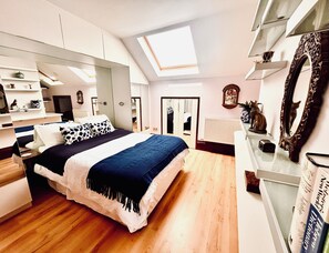 A bedroom with a large bed, skylight, built-in wardrobe, and a mirror.