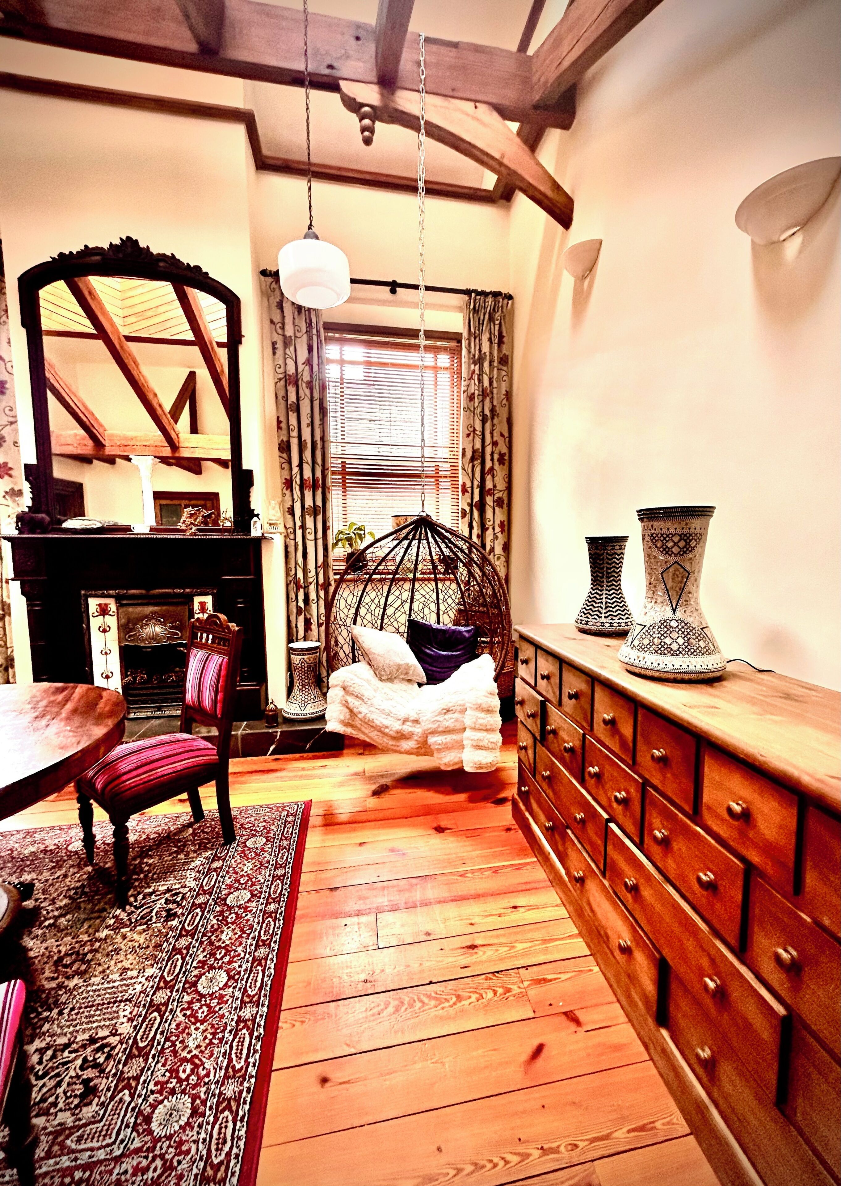 A room with a wooden floor, a dining table, a chair, a hanging chair, a dresser, and a mirror.