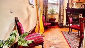 A traditional room with wooden flooring, a harp, red upholstered chairs, and a fireplace.