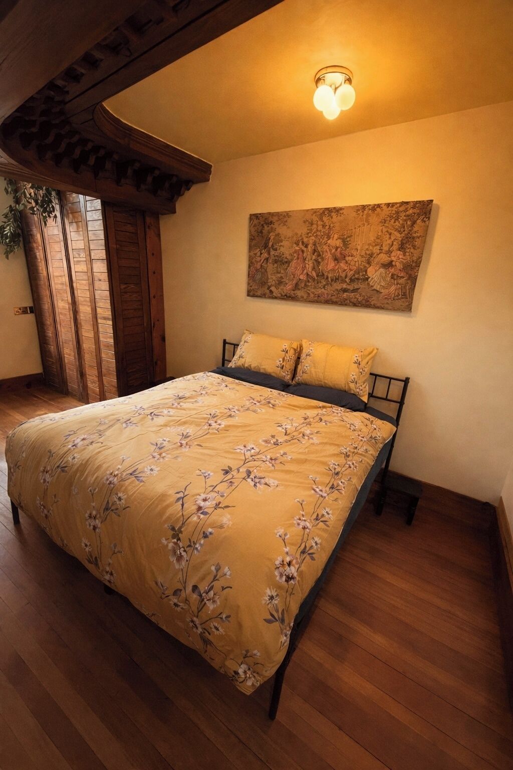 A bedroom with a wooden bed, a floral bedspread, a painting on the wall, and a wooden ceiling.
