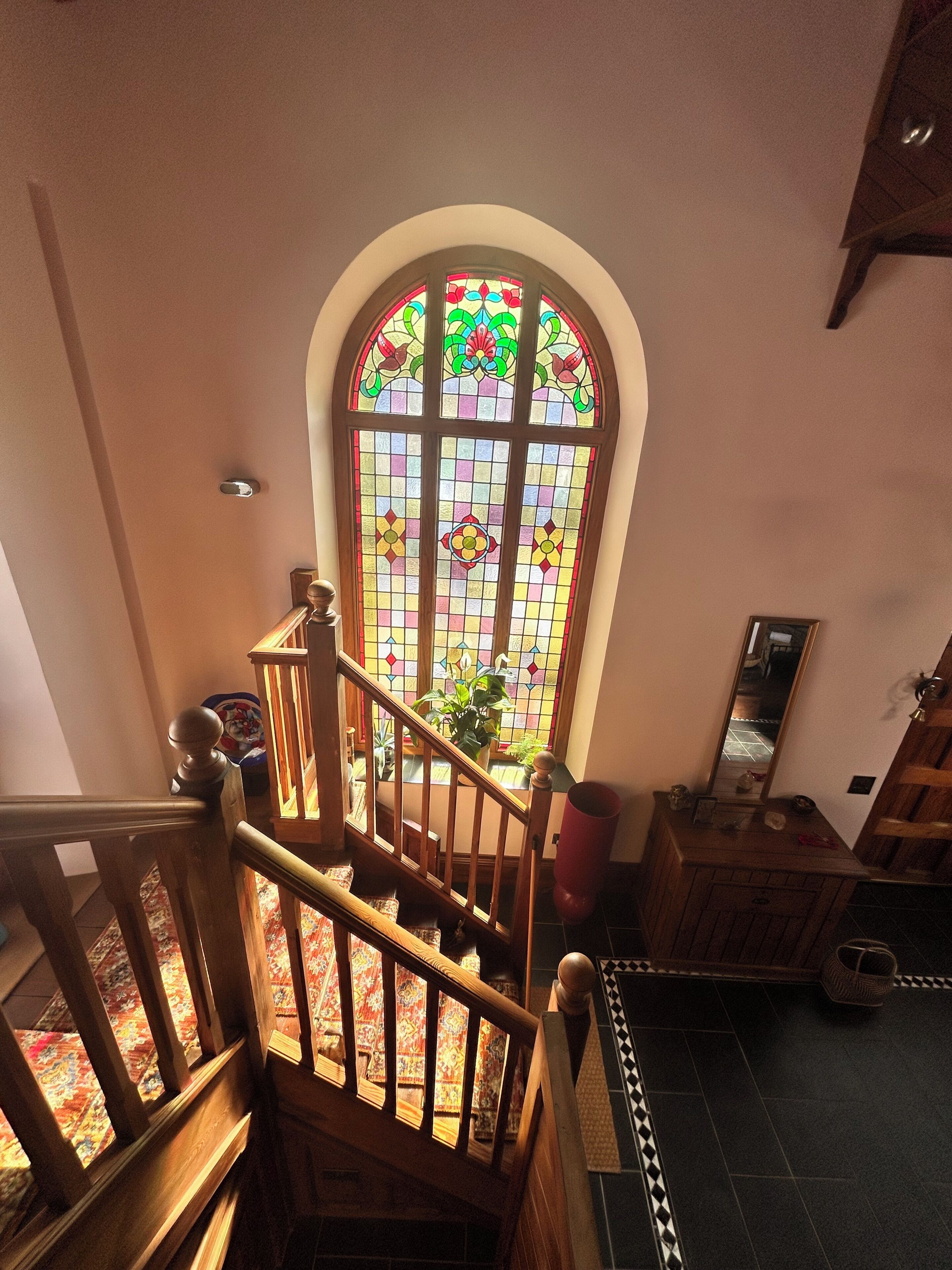 A staircase with a wooden handrail leading to a room with a large stained glass window.