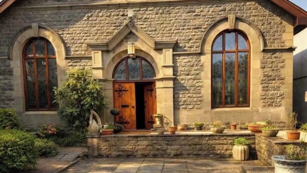 A stone building with a pitched roof, arched windows, and a central entrance.