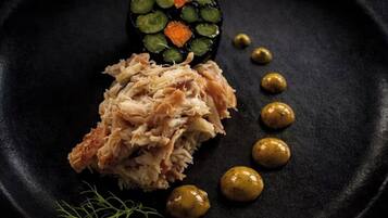 A plate with shredded meat, a slice of vegetable, and small round items, possibly olives, on a dark plate.