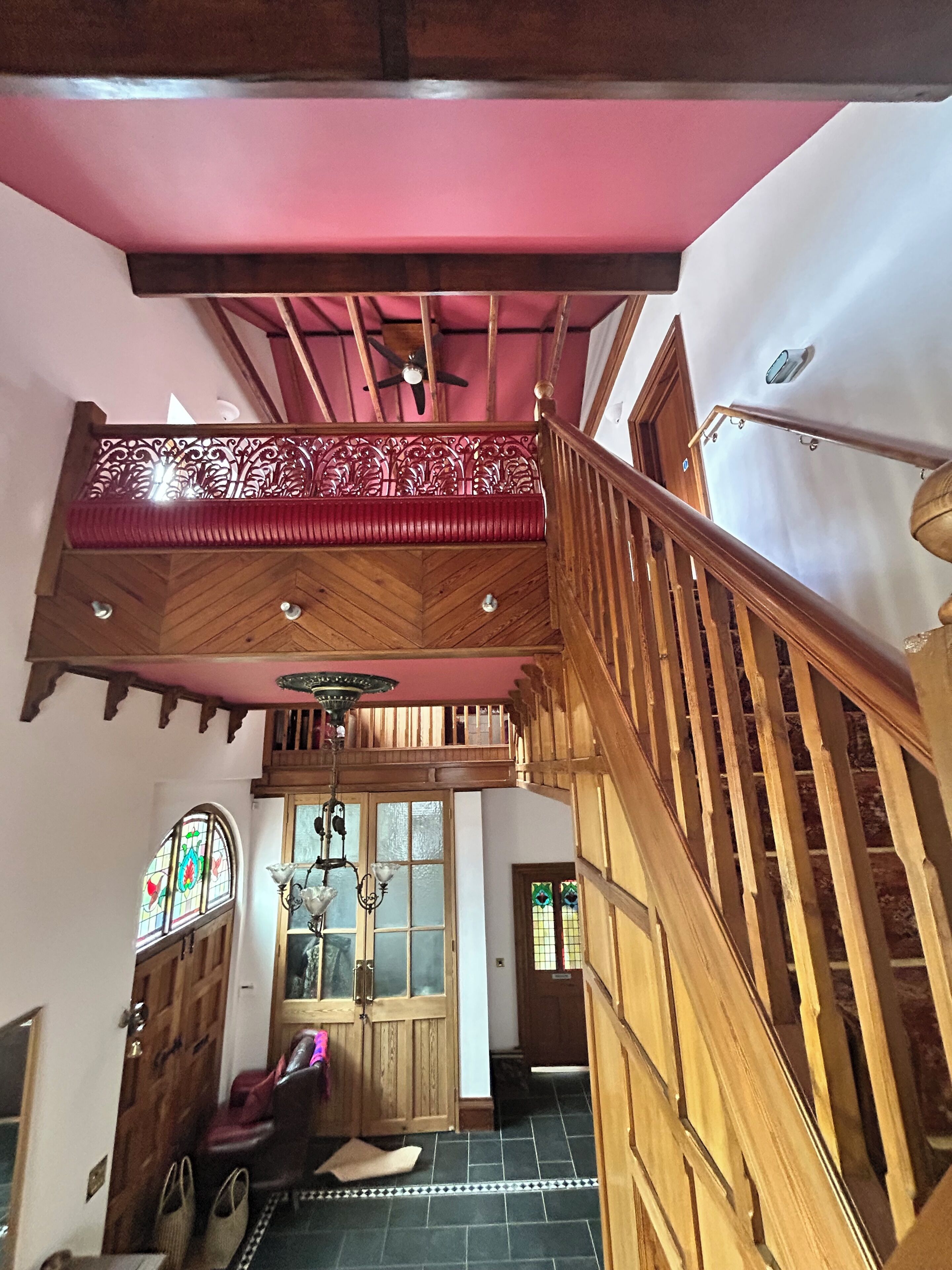 A wooden staircase with a red railing, a chandelier, and a wooden door with glass panels.