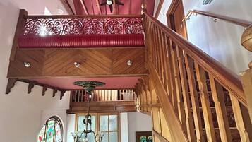 A wooden staircase with a red railing, a chandelier, and a wooden door with glass panels.