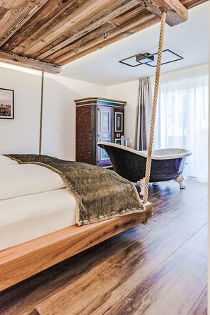 Ein Zimmer mit einem Bett, einer Badewanne im Vintage-Stil, einer Holzbalkendecke und einem klassischen Schrank.