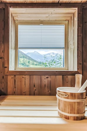 Ein Holzinnenraum mit einem Fenster, das eine gebirgige Landschaft zeigt, einer Holzwanne und einem weißen Gegenstand auf der Fensterbank.