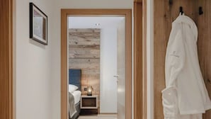 A hallway leading to a bedroom with a wooden floor, a bed, a nightstand, and a robe hanging on a wooden door. - 3A mit Tradition/am Bach by Interhome (Bad Hofgastein)