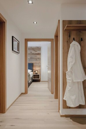 Ein Flur, der zu einem Schlafzimmer mit Holzboden, einem Bett, einem Nachttisch und einem an einer Holztür hängenden Bademantel führt.