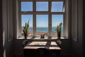 A dining area with a table, chairs, and a view of the ocean through a window. - Located right on the beach (Seaford)