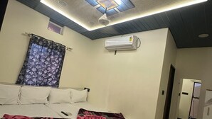 Un dormitorio con cama, ventilador de techo, unidad de aire acondicionado y ventana con cortina.