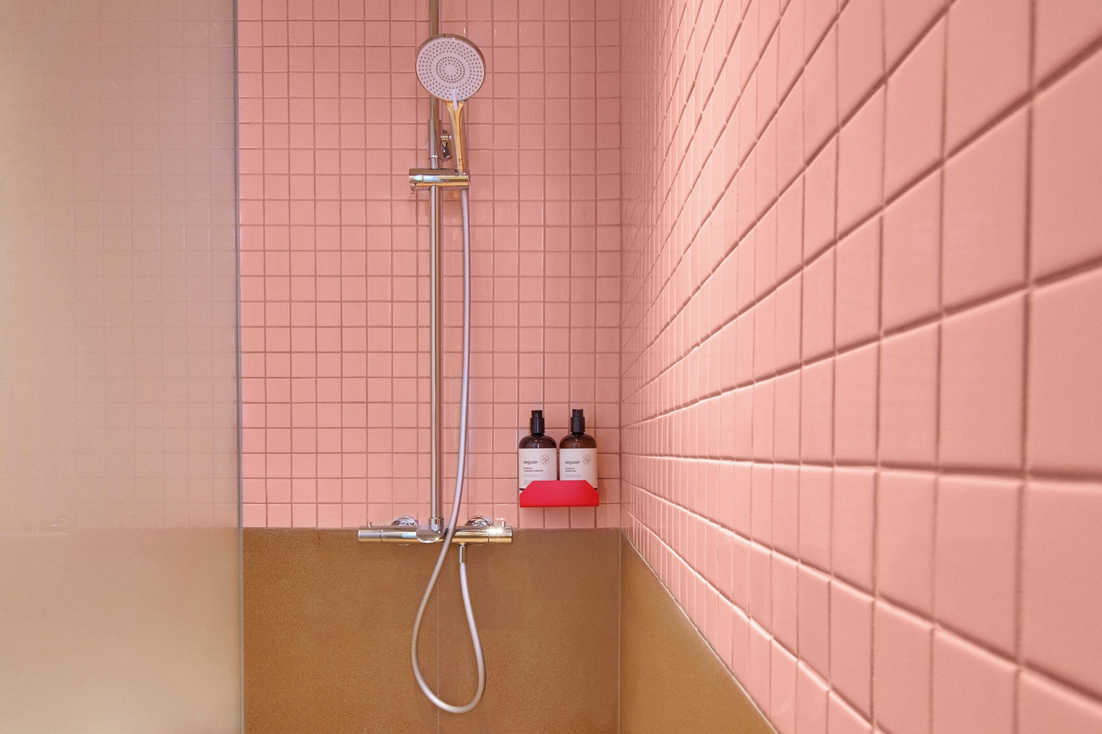 A shower with a handheld showerhead, a wall-mounted faucet, and two bottles of shampoo and conditioner on a shelf.