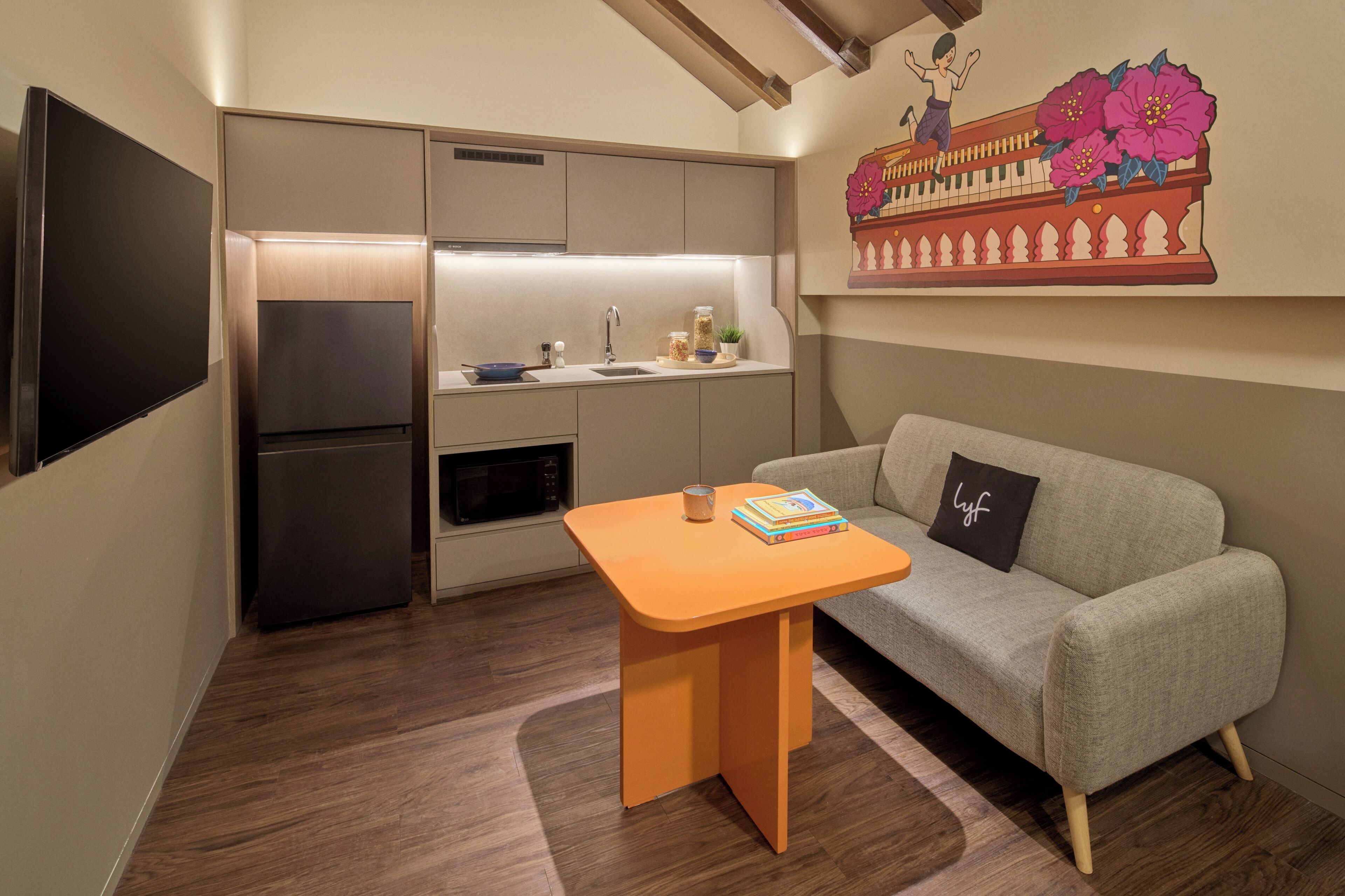 A compact living space with a kitchenette, a sofa, a small table, and a flat-screen TV.