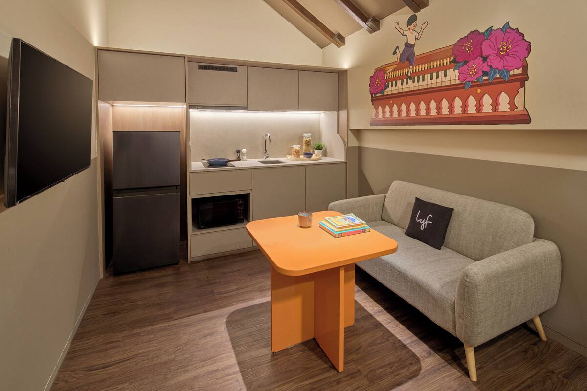 Een knus woongedeelte met een kitchenette, een bank, een kleine tafel en een flatscreen televisie.