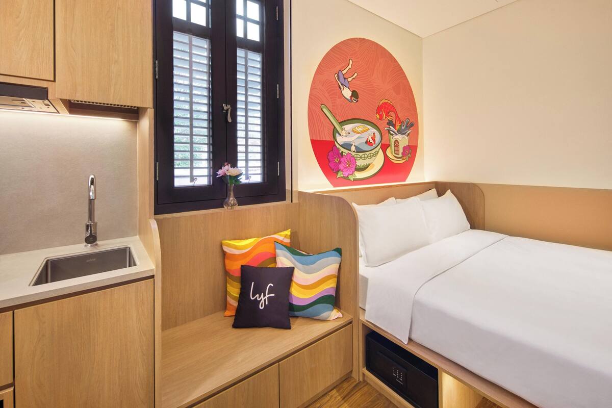 Een kleine kamer met een bed, een klein wastafeltje en een raam met zonwering.