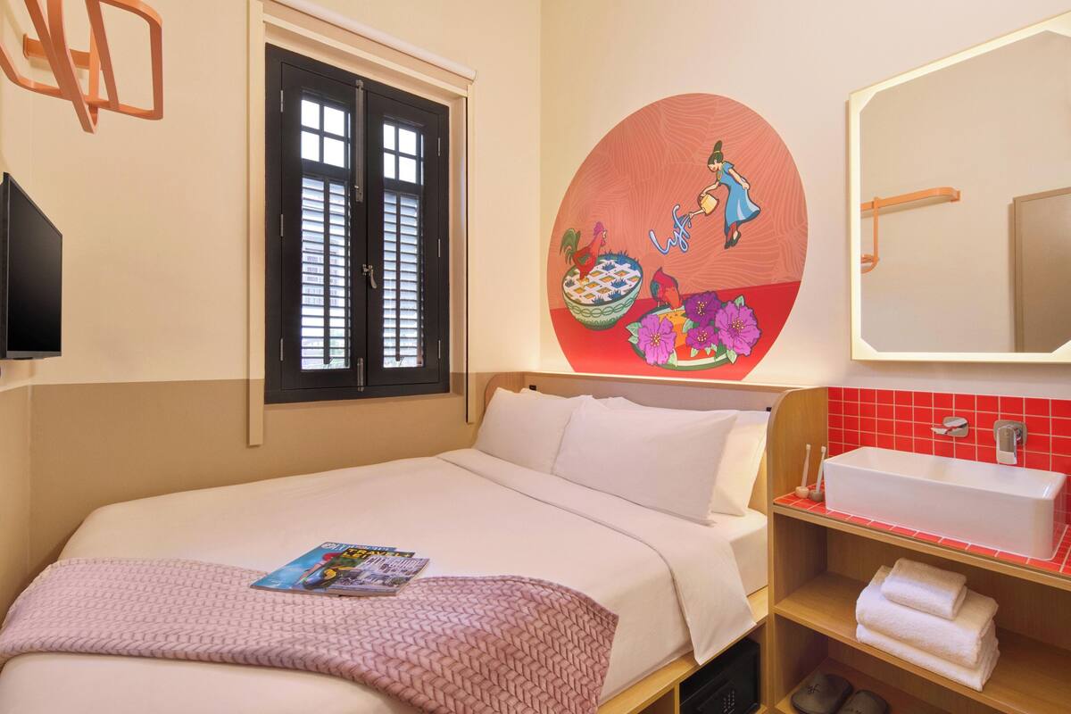 Hotelkamer met een bed, een wandtelevisie, een raam met zonwering, een badkamer met wastafel en spiegel, en een decoratief kunstwerk aan de muur.