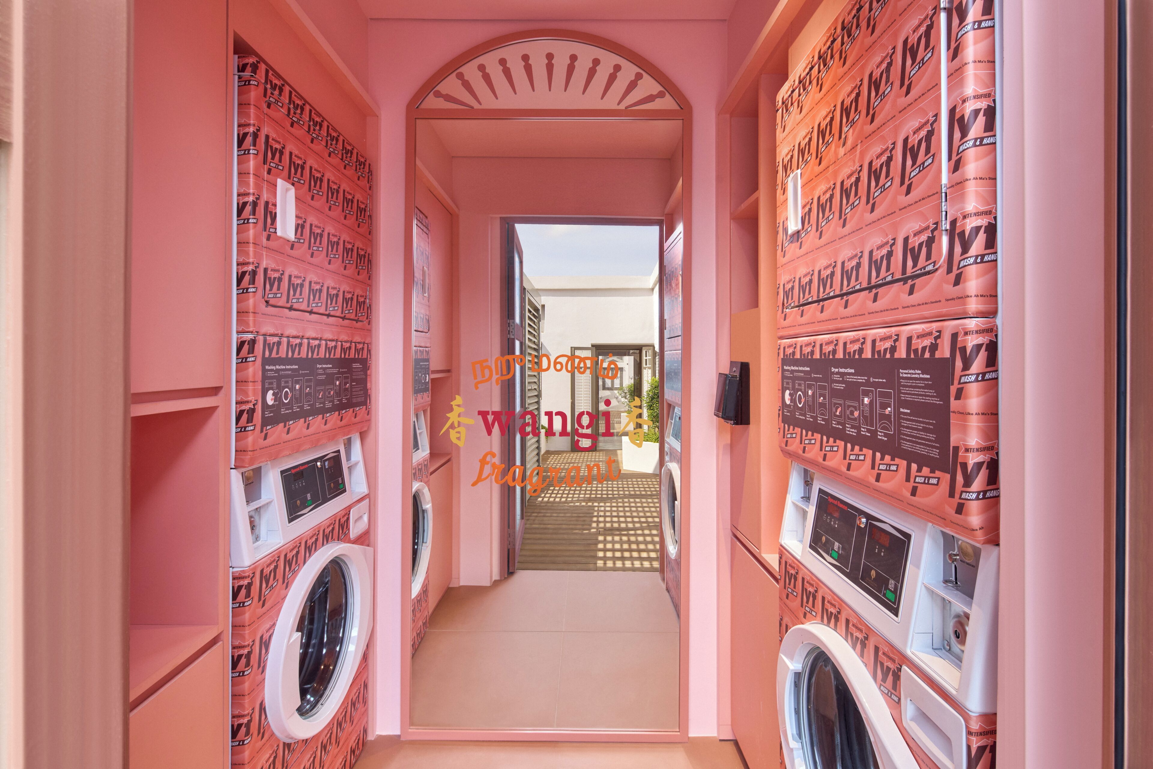 A laundry room with multiple washing machines and dryers, a tiled floor, and a pink wall.