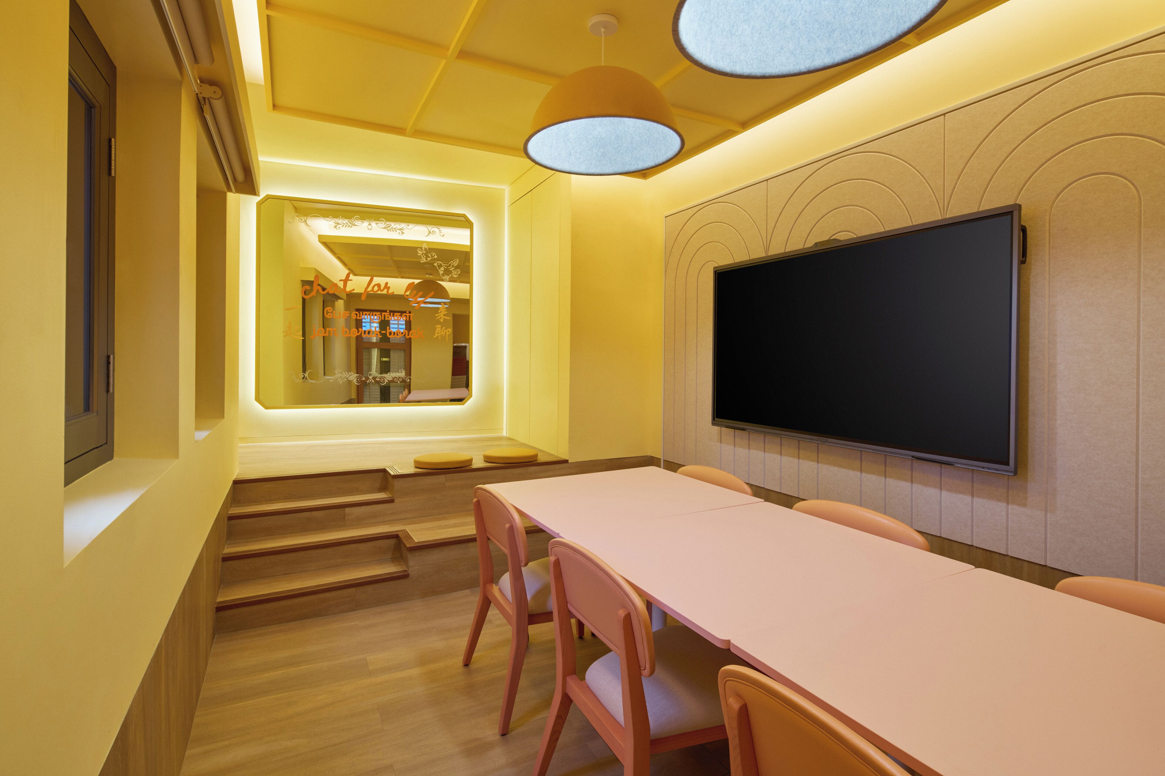 Un salón de conferencias con una larga mesa, sillas, un televisor de pantalla plana y una escalera que sube a un nivel superior.