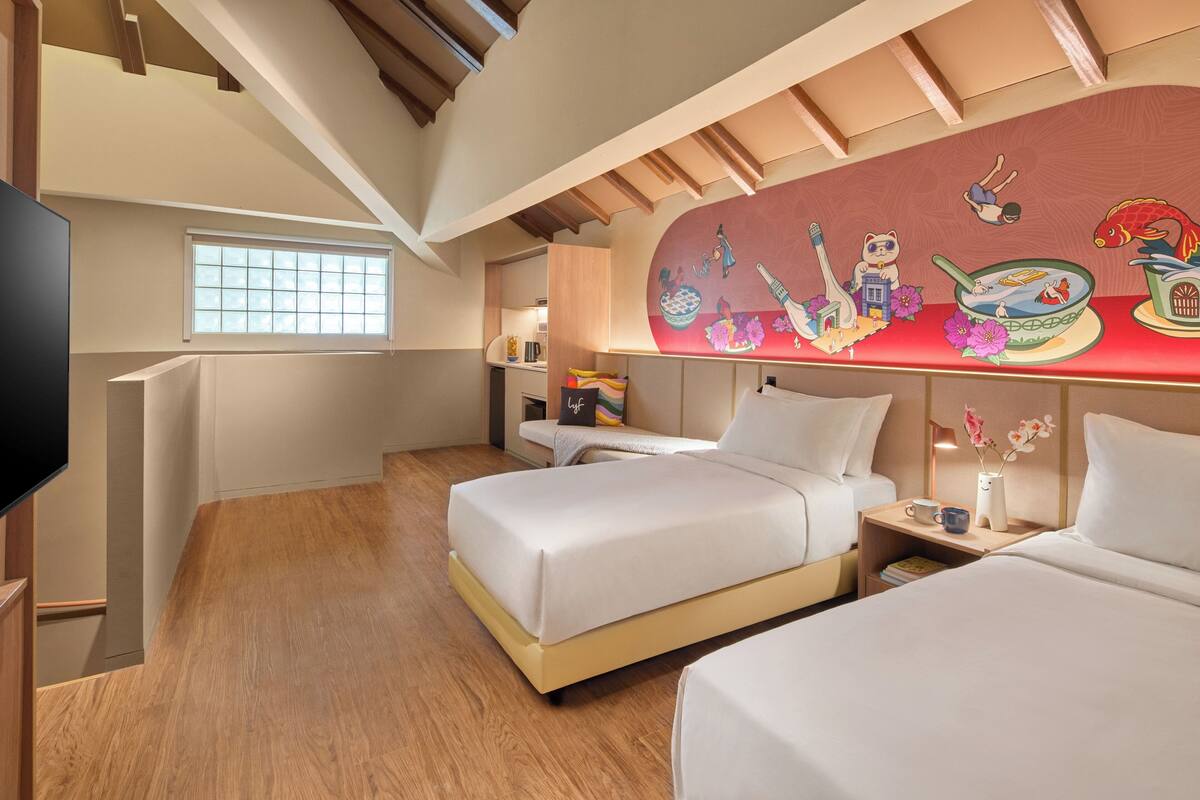Een hotelkamer met twee bedden, een televisie, een raam en een muurschildering.
