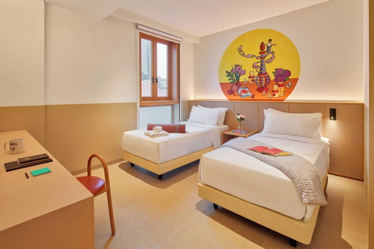 Hotelkamer met twee bedden, een bureau, een stoel, een raam en een schilderij aan de muur.