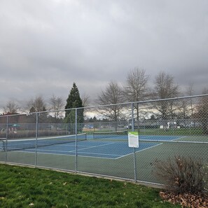 A fenced tennis court with a sign indicating dogs may be off-leash.