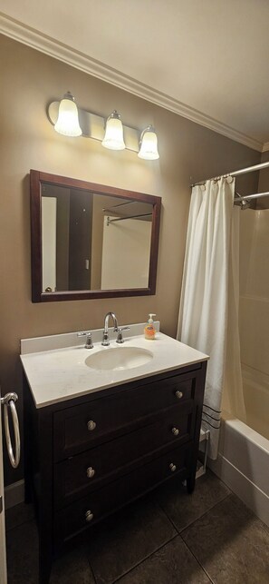 A bathroom with a dark vanity, a large mirror, a white sink, and a shower curtain.