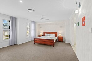 Une chambre à coucher avec un lit en bois, deux tables de chevet avec des lampes, un ventilateur de plafond et une fenêtre avec des stores.