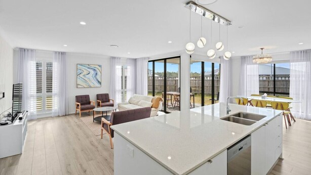 A modern kitchen with a central island, a dining area with yellow chairs, and a living room with a sofa and chairs.