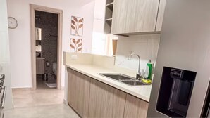 A kitchen with a sink, a refrigerator, and a door leading to another room.