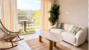 A living room with a white sofa, a rocking chair, a coffee table, a potted plant, and a balcony with a table and chairs.