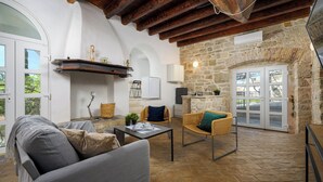 Un salon chaleureux avec un mur en pierre, des poutres apparentes, un canapé, des fauteuils et une table.