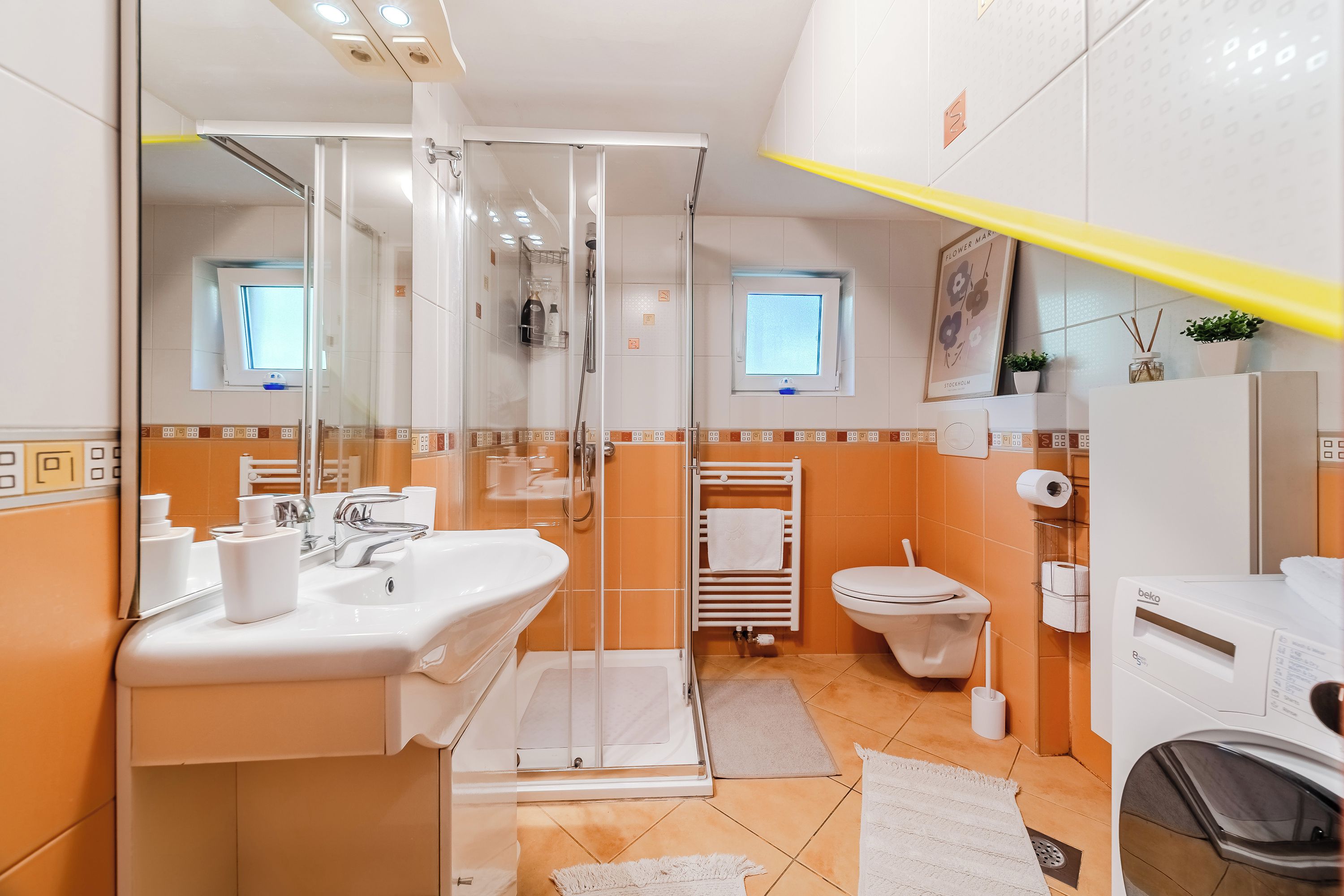 Un bagno moderno con box doccia in vetro, lavandino, water e lavatrice.