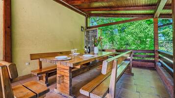 Una mesa de madera al aire libre con bancos, una planta en maceta y una ventana con vistas a la vegetación.